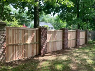 Wooden privacy fence with brick posts along a leafy yard