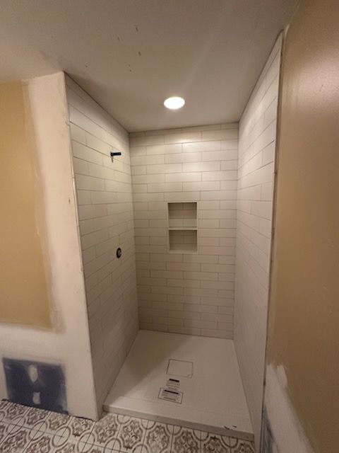 Empty tiled walk-in shower with built-in niche and recessed ceiling light
