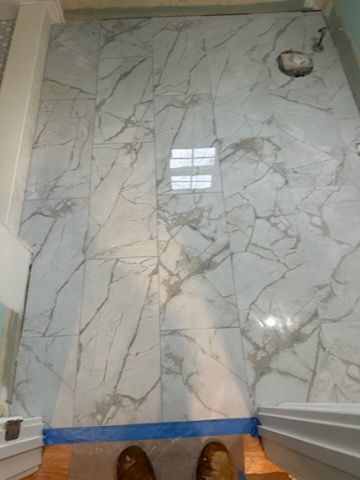 Marble-patterned tile floor with blue tape along the edge and a small hole in the upper right corner