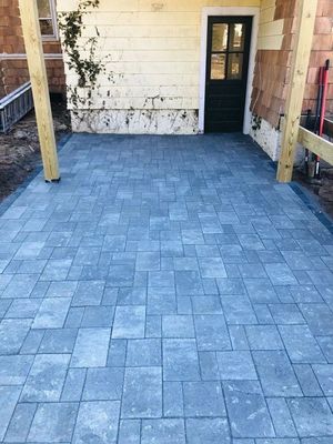 Blue-gray stone patio with wooden posts and a black door leading to a house entrance
