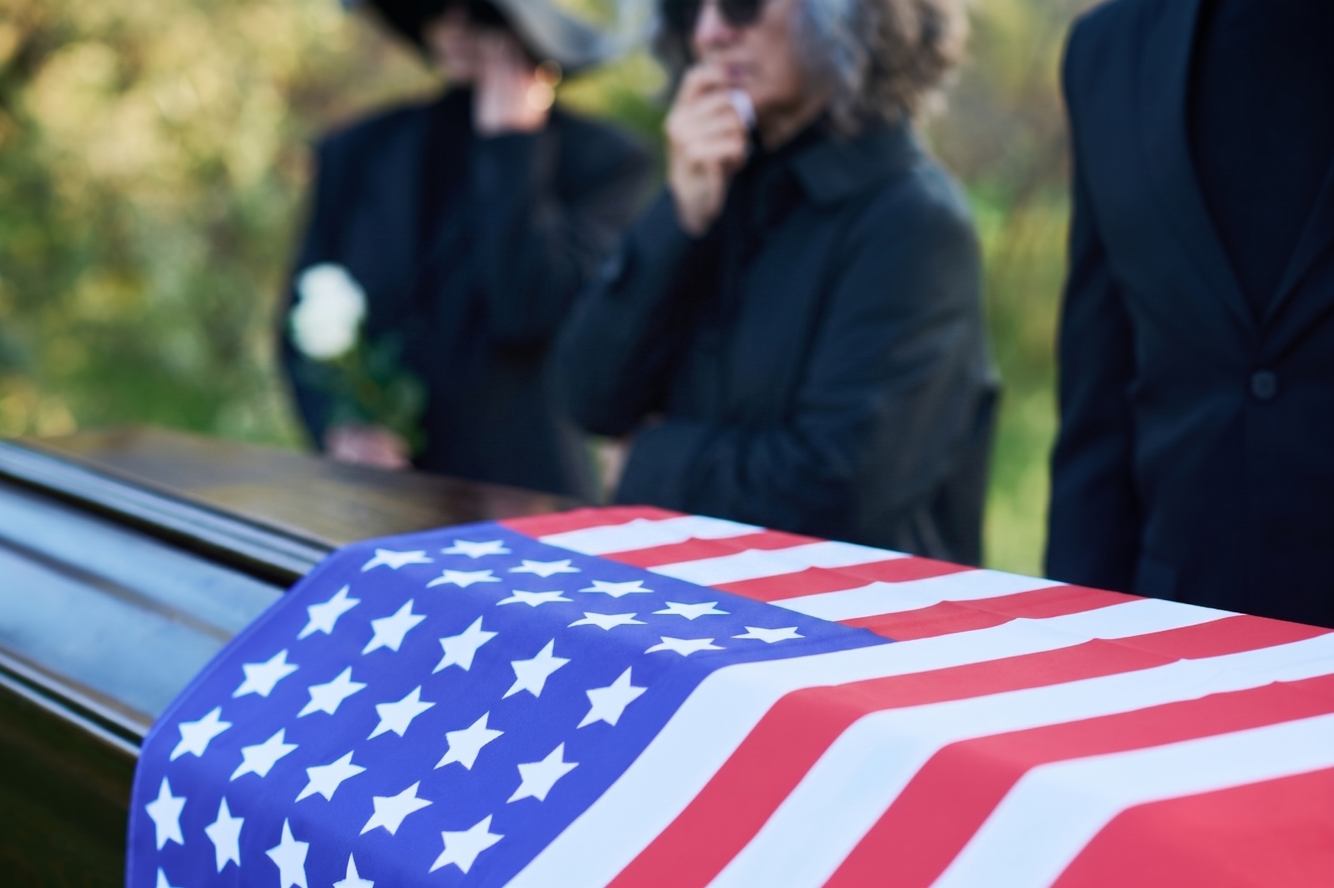 A woman is holding an american flag and a rose at a funeral.