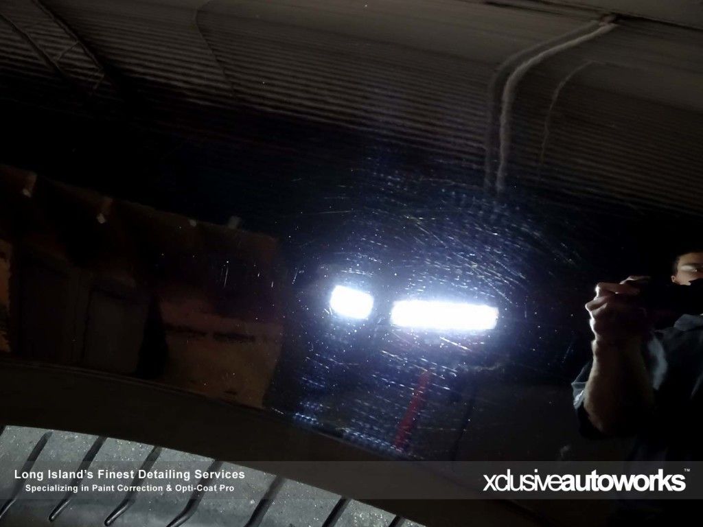 A person is taking a picture of a car with xclusiveautoworks written on the bottom