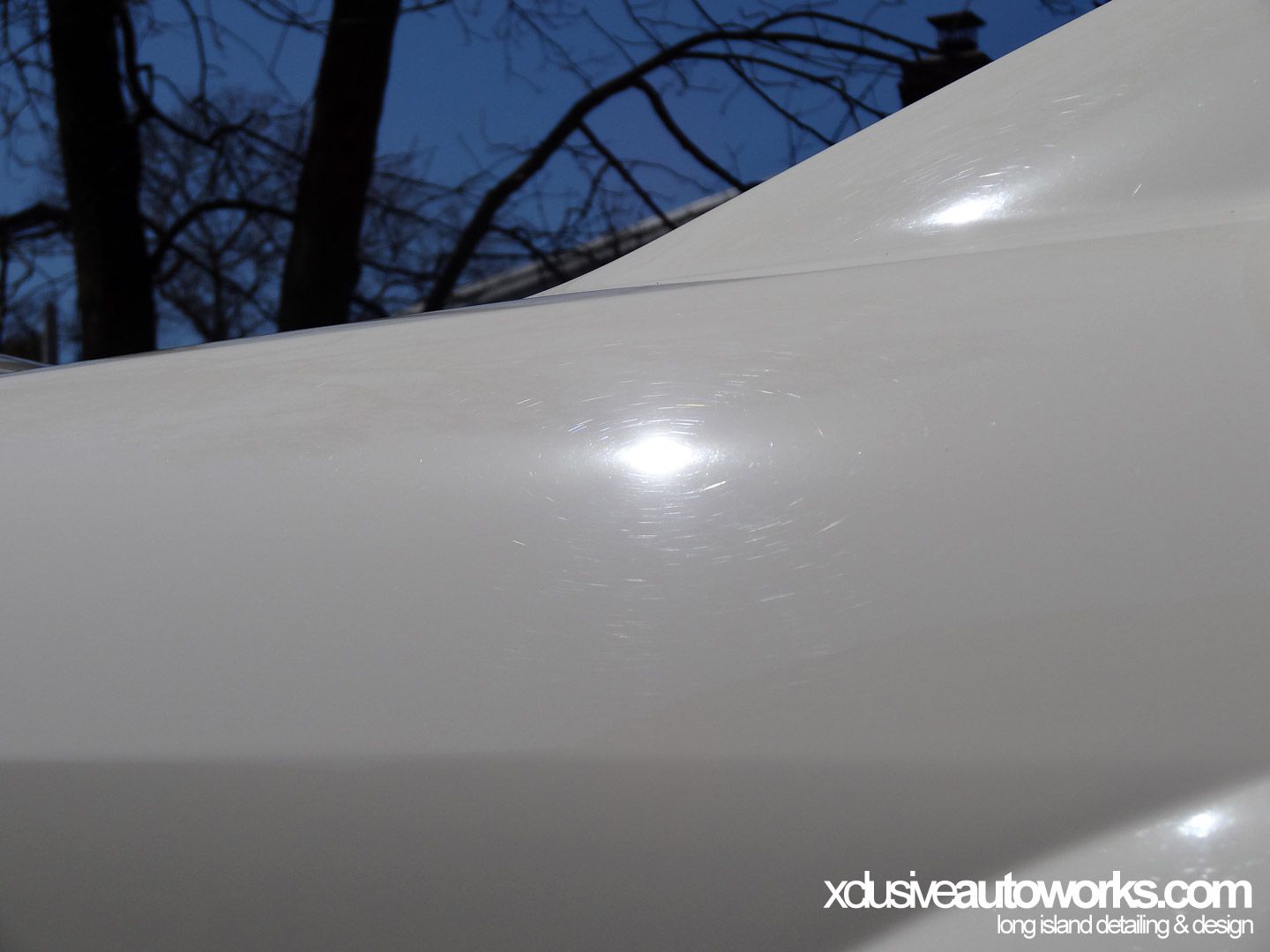 A close up of a white car with xdusveautoworks.com written on the bottom