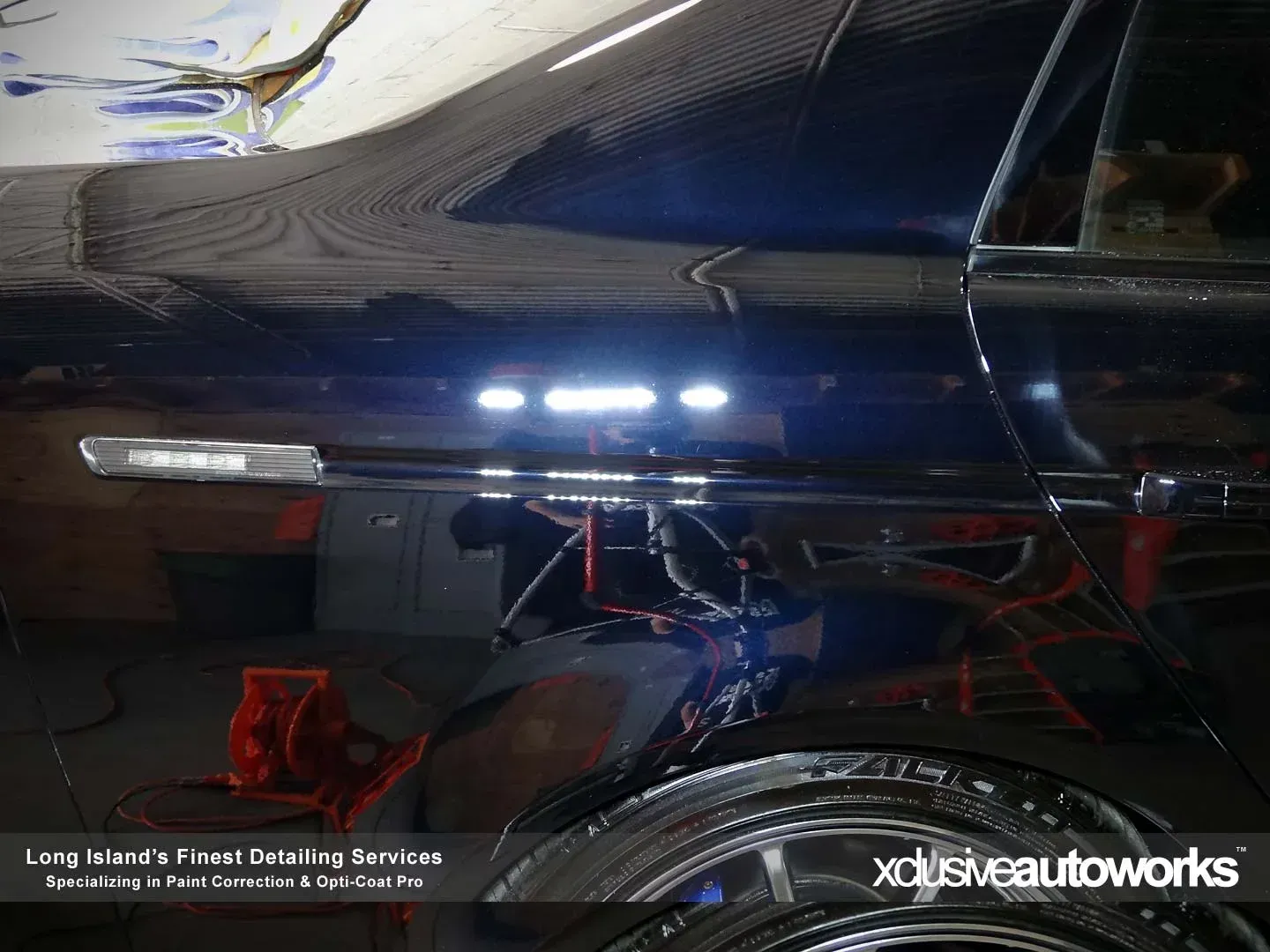 A black car is sitting in a garage being polished by xclusive autoworks.