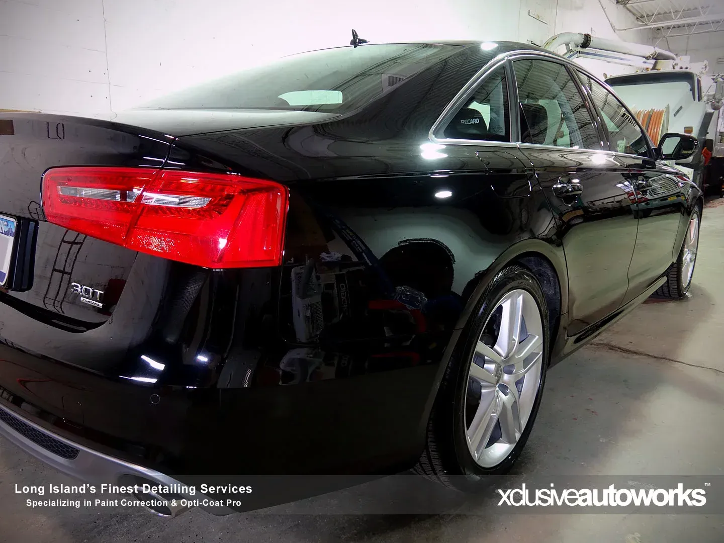 A black car with a red tail light is parked in a garage.