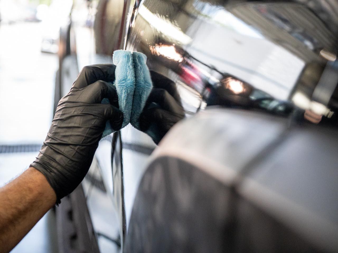 A man is cleaning the hood of a black car with a cloth.