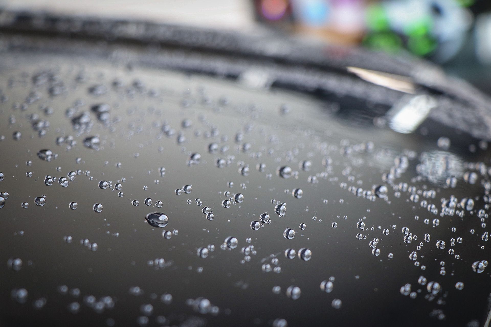 A man is cleaning the hood of a black car with a cloth.