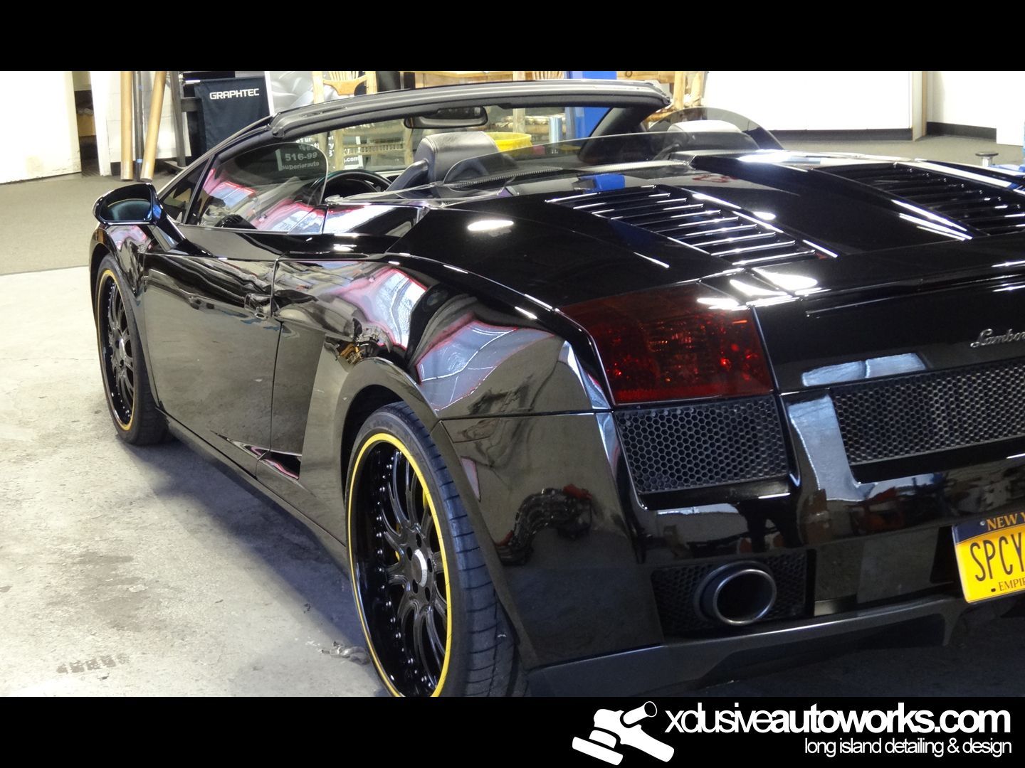 A black sports car is parked in a garage with the website xdusveautoworks.com on the bottom