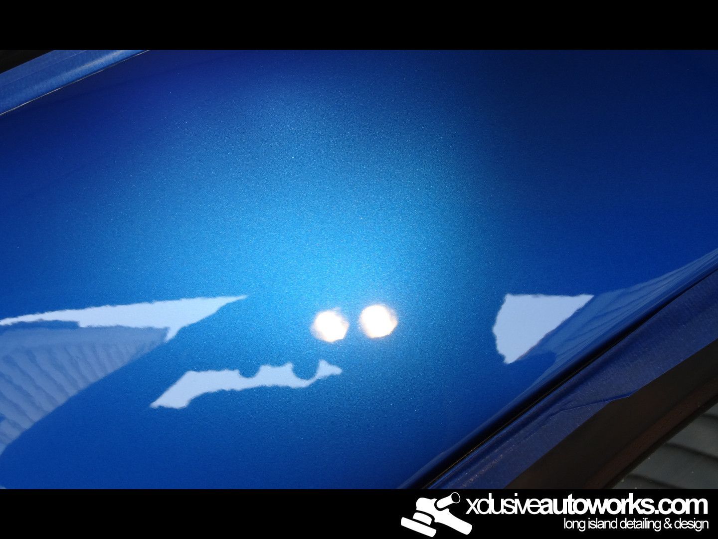 A close up of a blue car with xclusiveautoworks.com written on the bottom