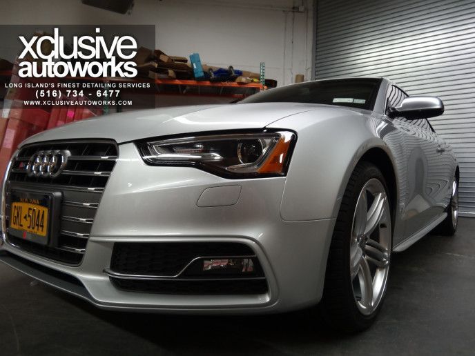A silver car is parked in front of a sign that says xclusive autoworks