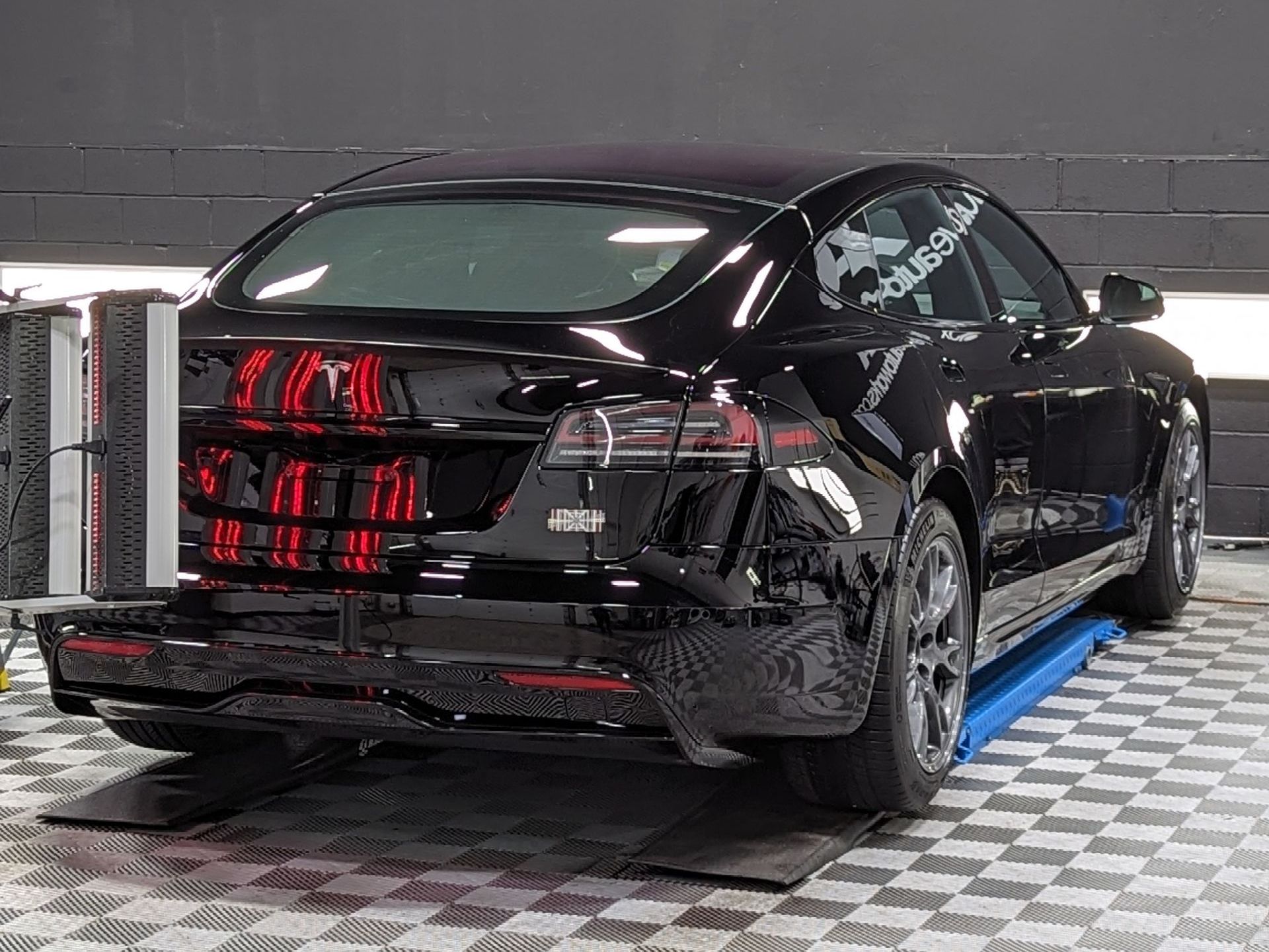 A black tesla model s is sitting on top of a blue lift in a garage.