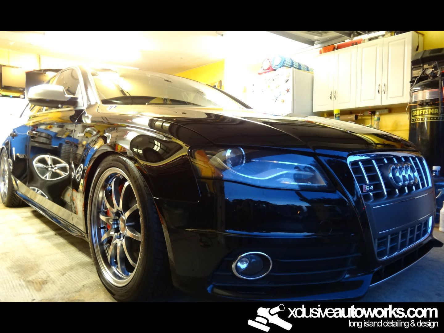 A black car is parked in a garage with xdusveautoworks.com written on the bottom