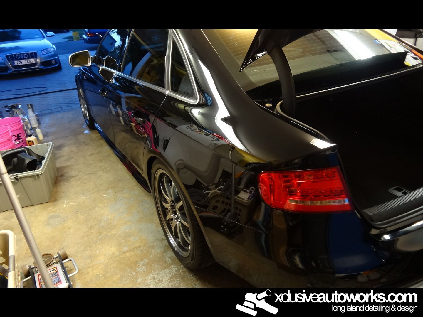 A black car is parked in a garage with the trunk open