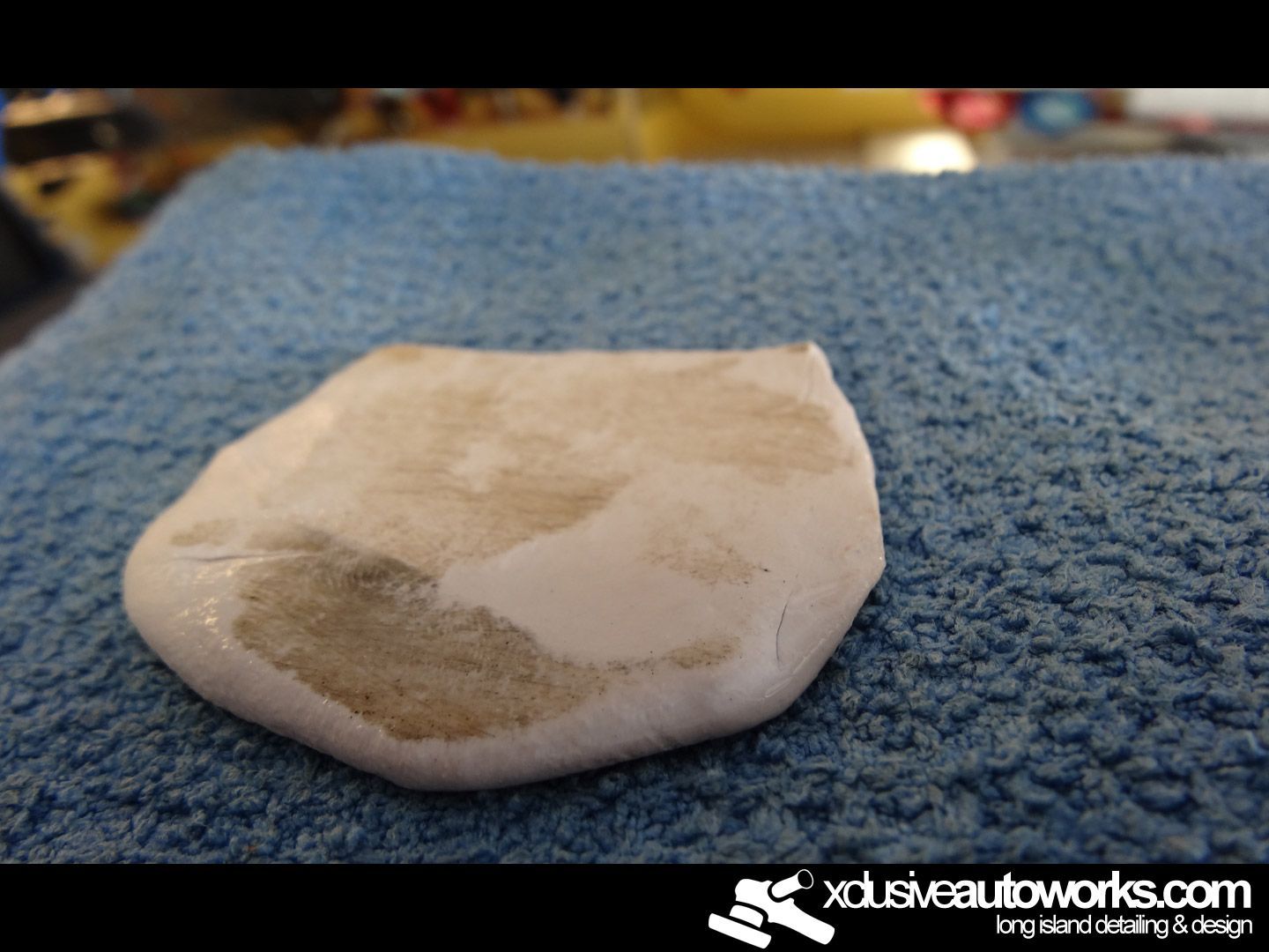 A piece of clay is sitting on a blue cloth with xdusveautoworks.com written on the bottom
