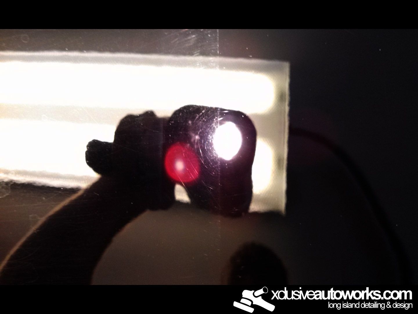 A person is holding a red object in front of a light that says xclusiveautoworks.com