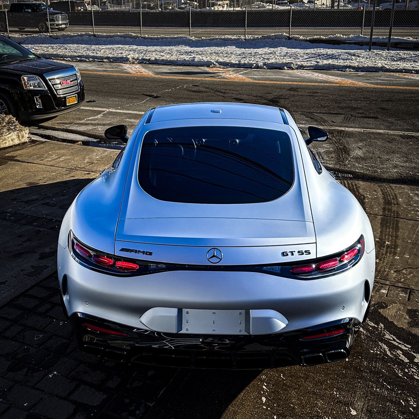 A silver Mercedes-AMG GT 55 sports car parked outdoors, viewed from the rear on a sunny day.