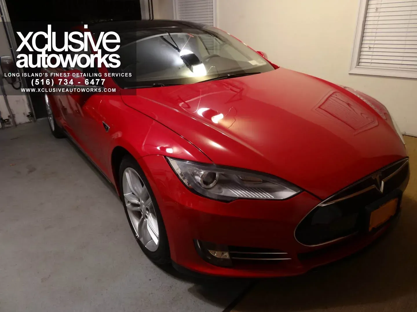 A red tesla model s is parked in a garage by xclusive autoworks