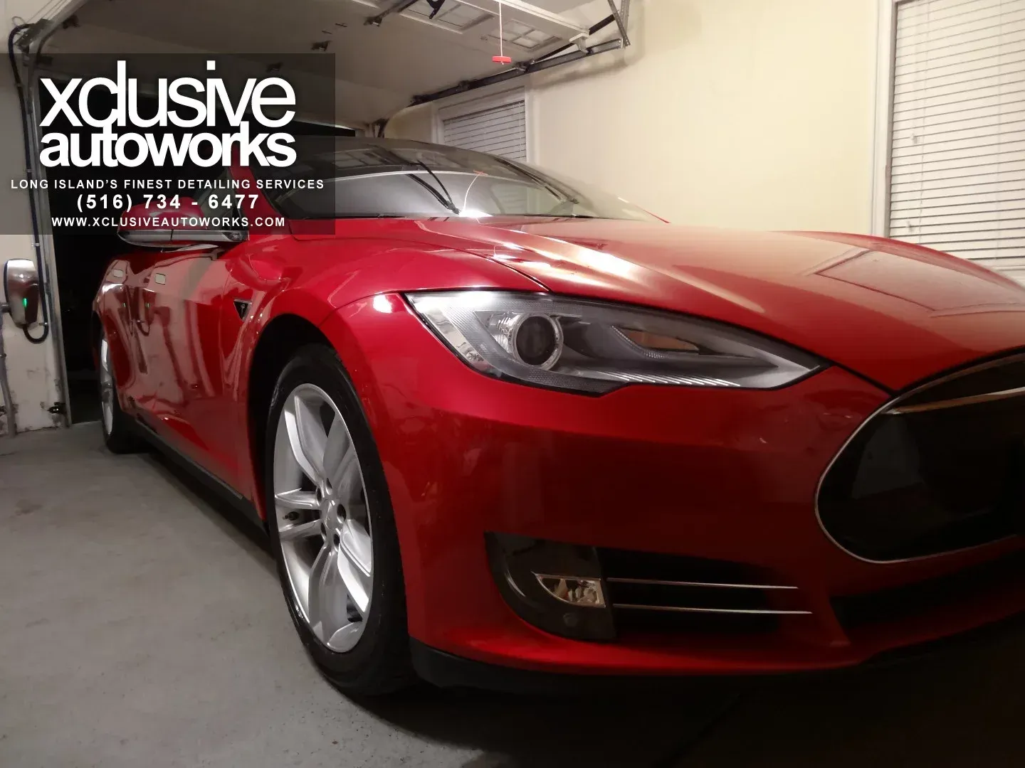 A red tesla model s is parked in a garage by xclusive autoworks