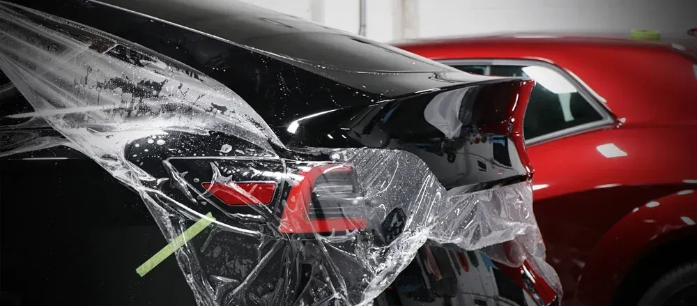 A man is cleaning the hood of a black car with a cloth.