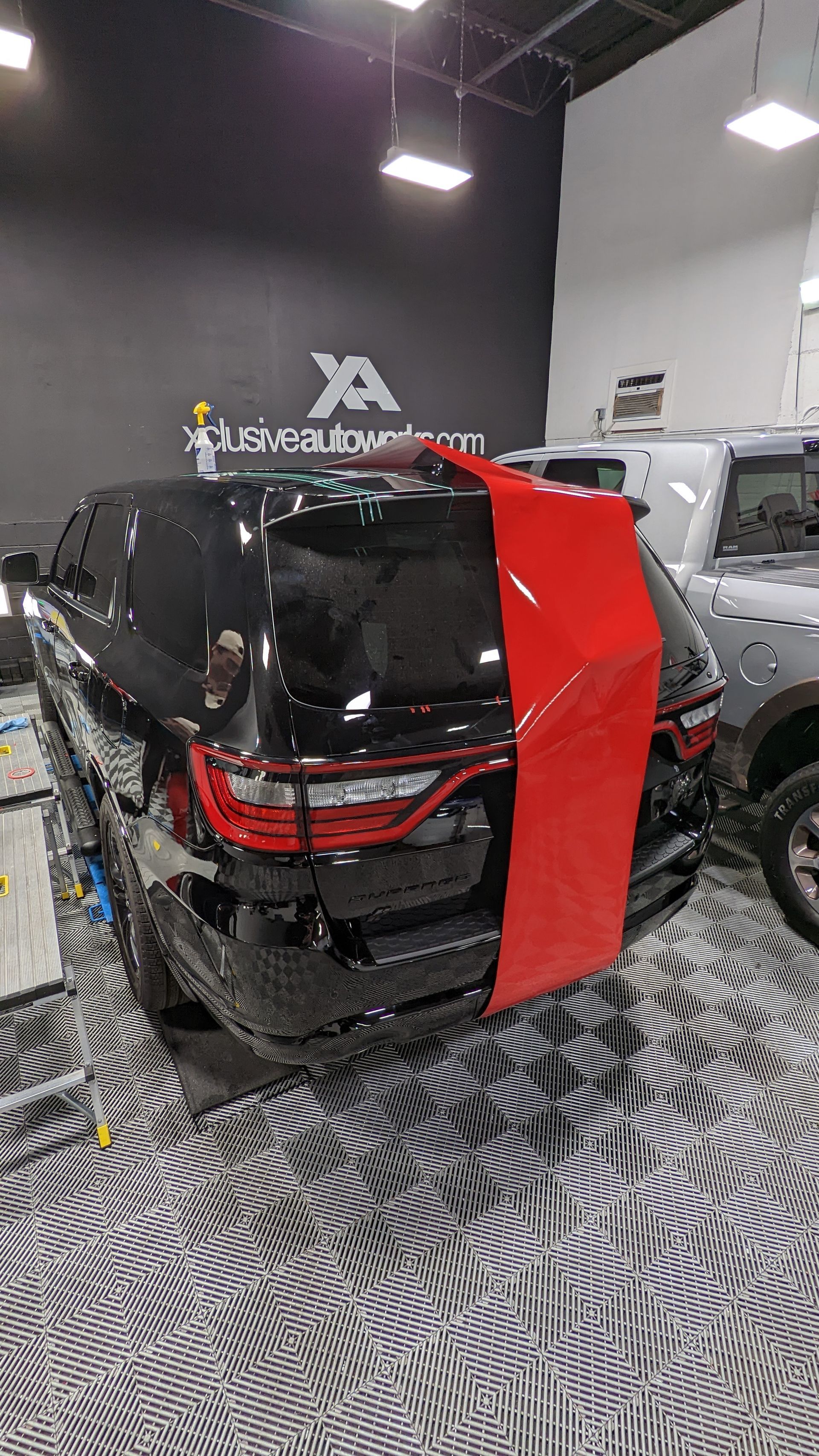 A partially wrapped black SUV in a garage features a large vertical stripe of bright red vinyl film on the rear.