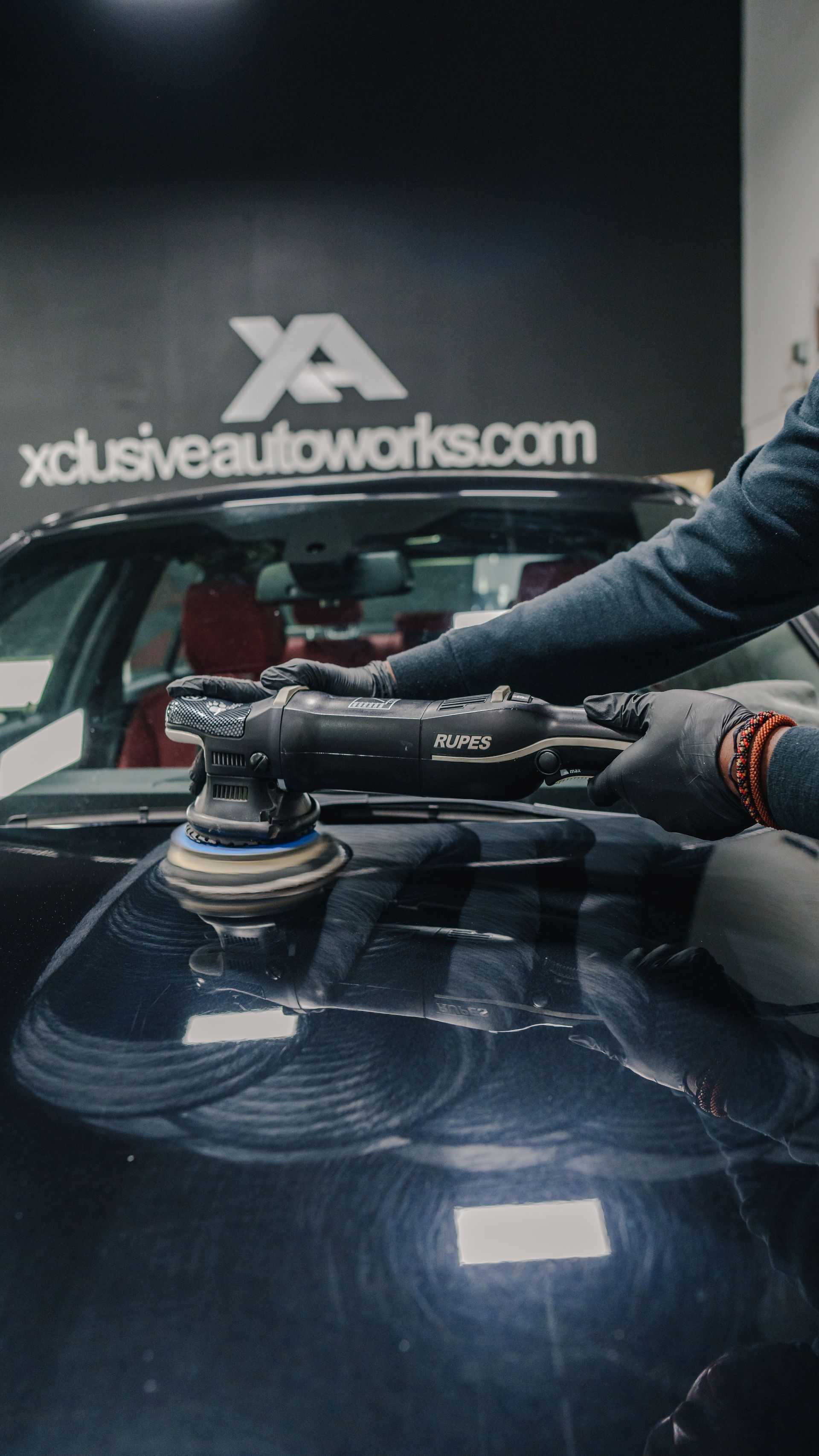 A man is polishing a black car with a machine.