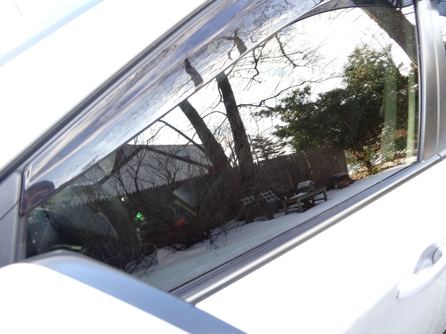 A white car with a reflection of trees in the window