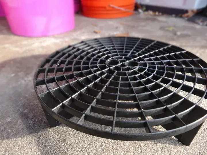 A black plastic grid sits on the ground in front of pink and orange buckets