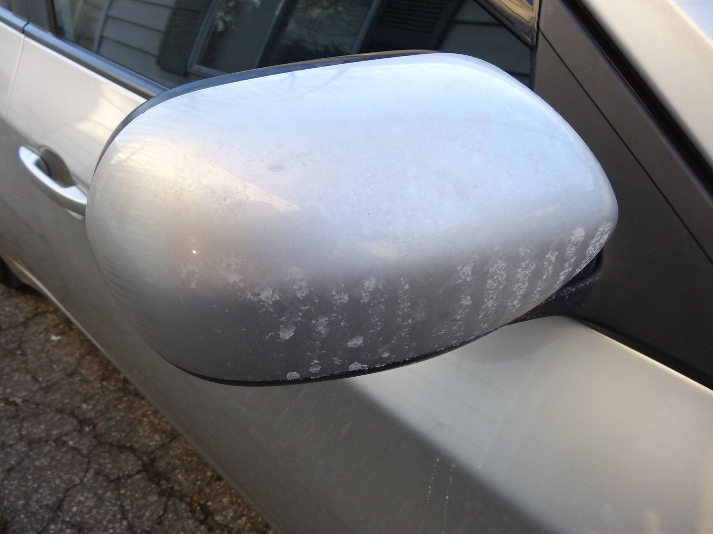 A silver car with a dirty rear view mirror