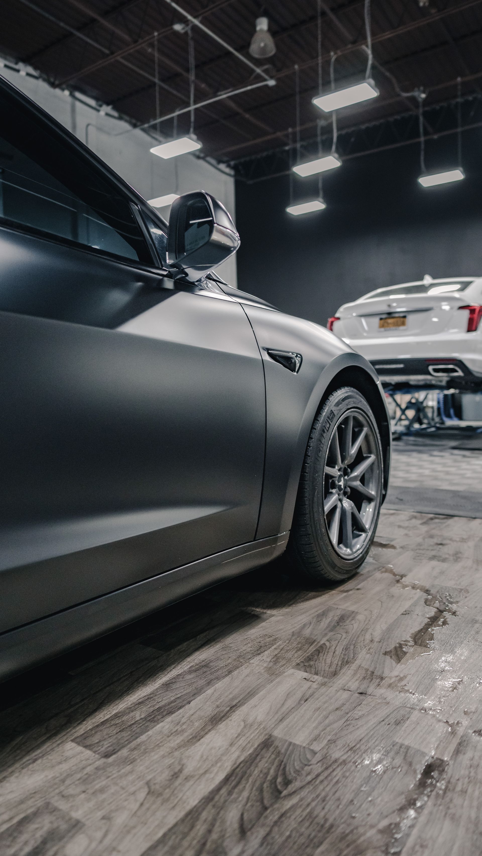 A tesla model 3 is parked in a garage next to another car.