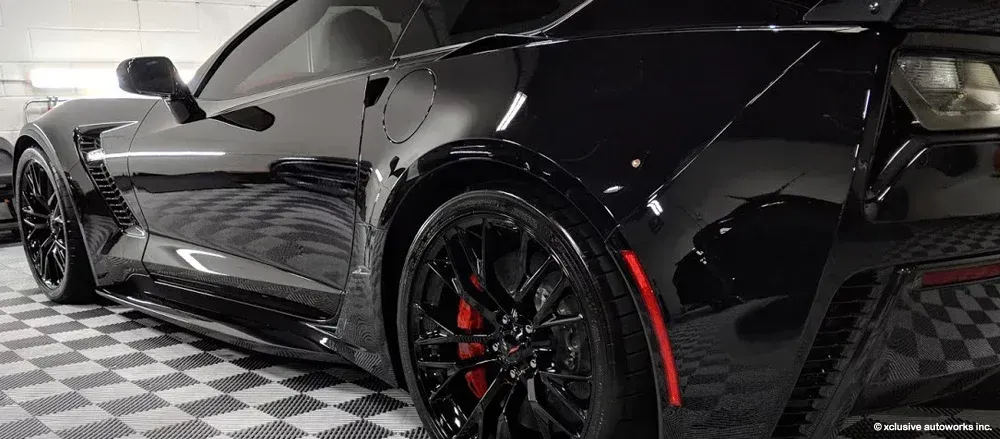 A black corvette zr1 is parked on a checkered floor in a garage.