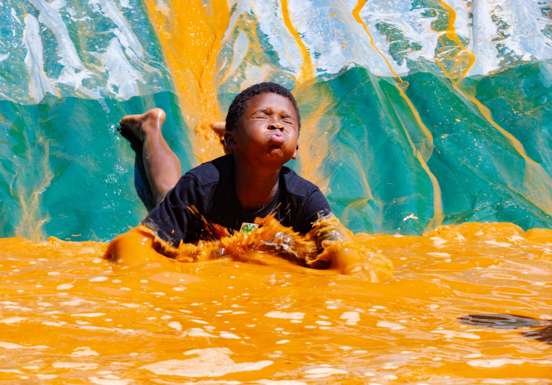 Child splashing in bright orange water, with a teal wave behind them