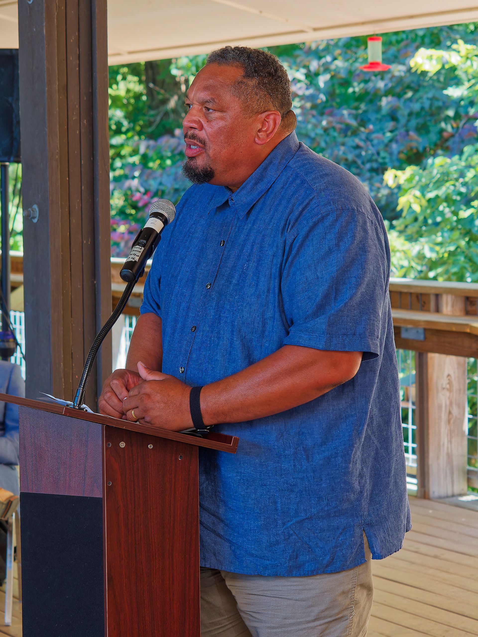 A man in a blue shirt is standing at a podium speaking into a microphone.