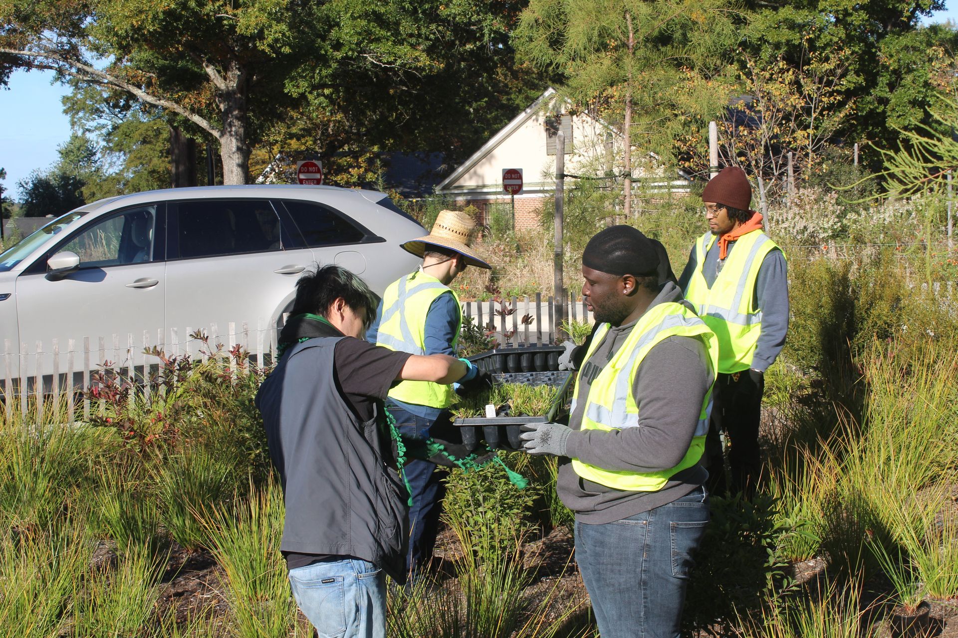 People in reflective vests talking on a roadside near a parked car and house in daylight