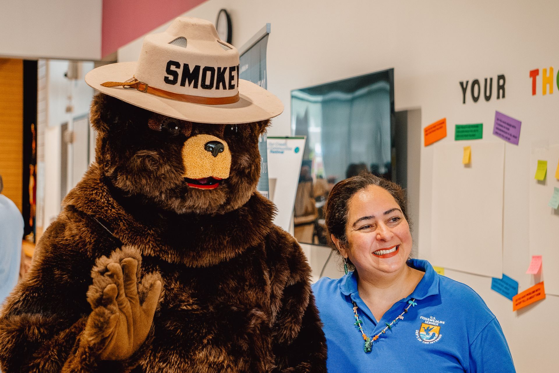 A woman is standing next to a smokey the bear mascot.