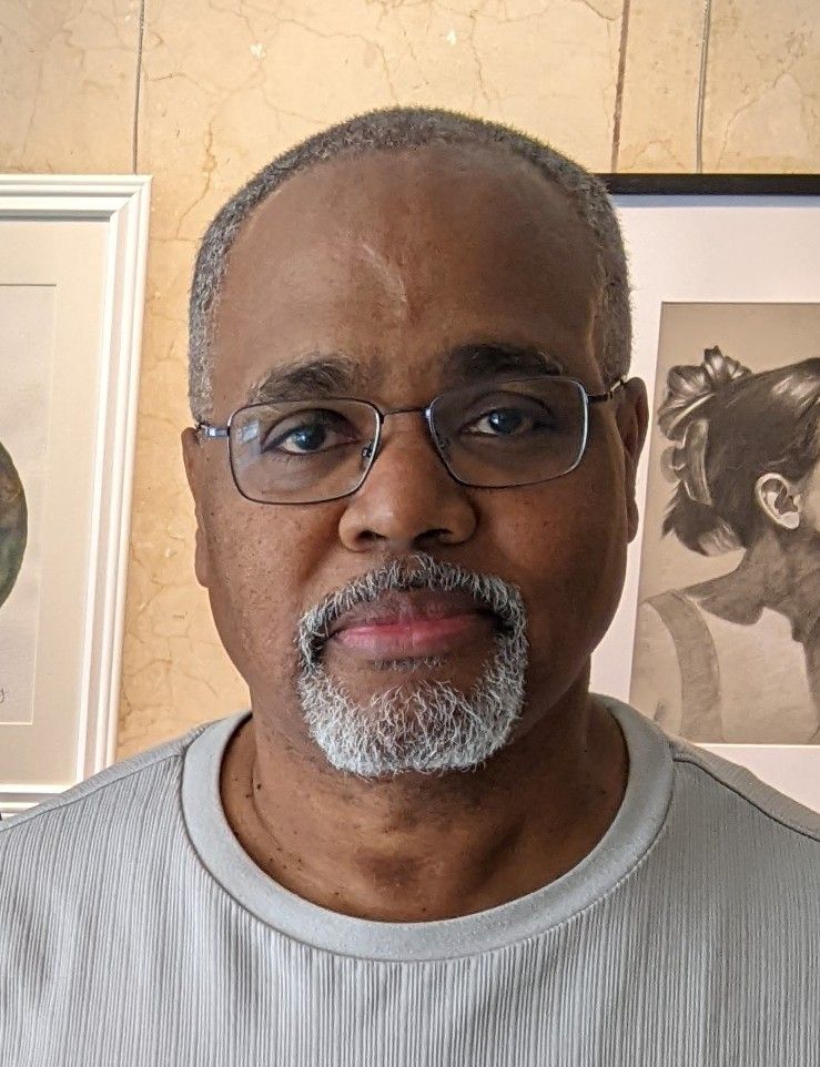 A man with glasses and a beard is standing in front of a picture.
