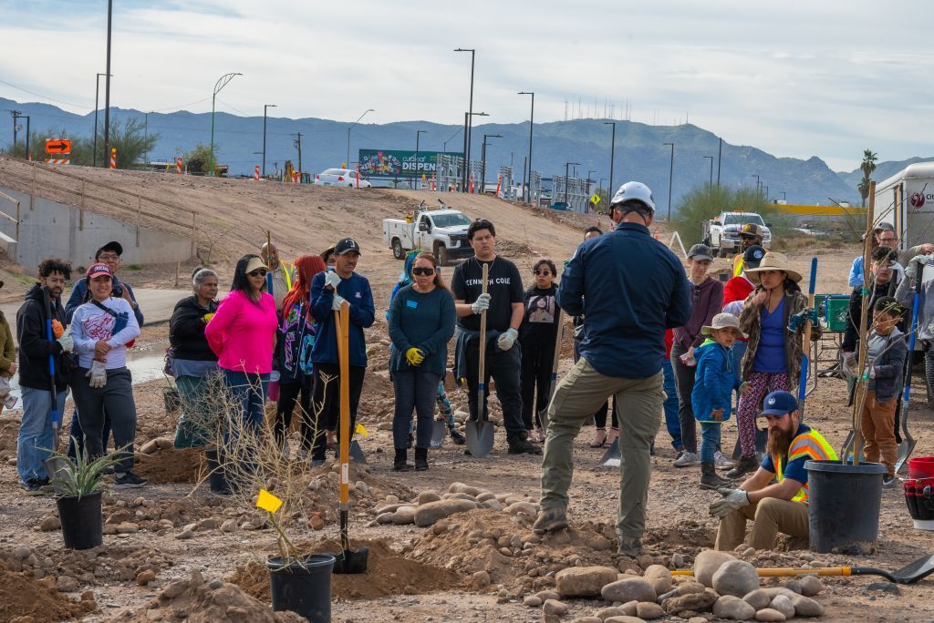 Community group planting trees in a muddy outdoor area with mountains in the background