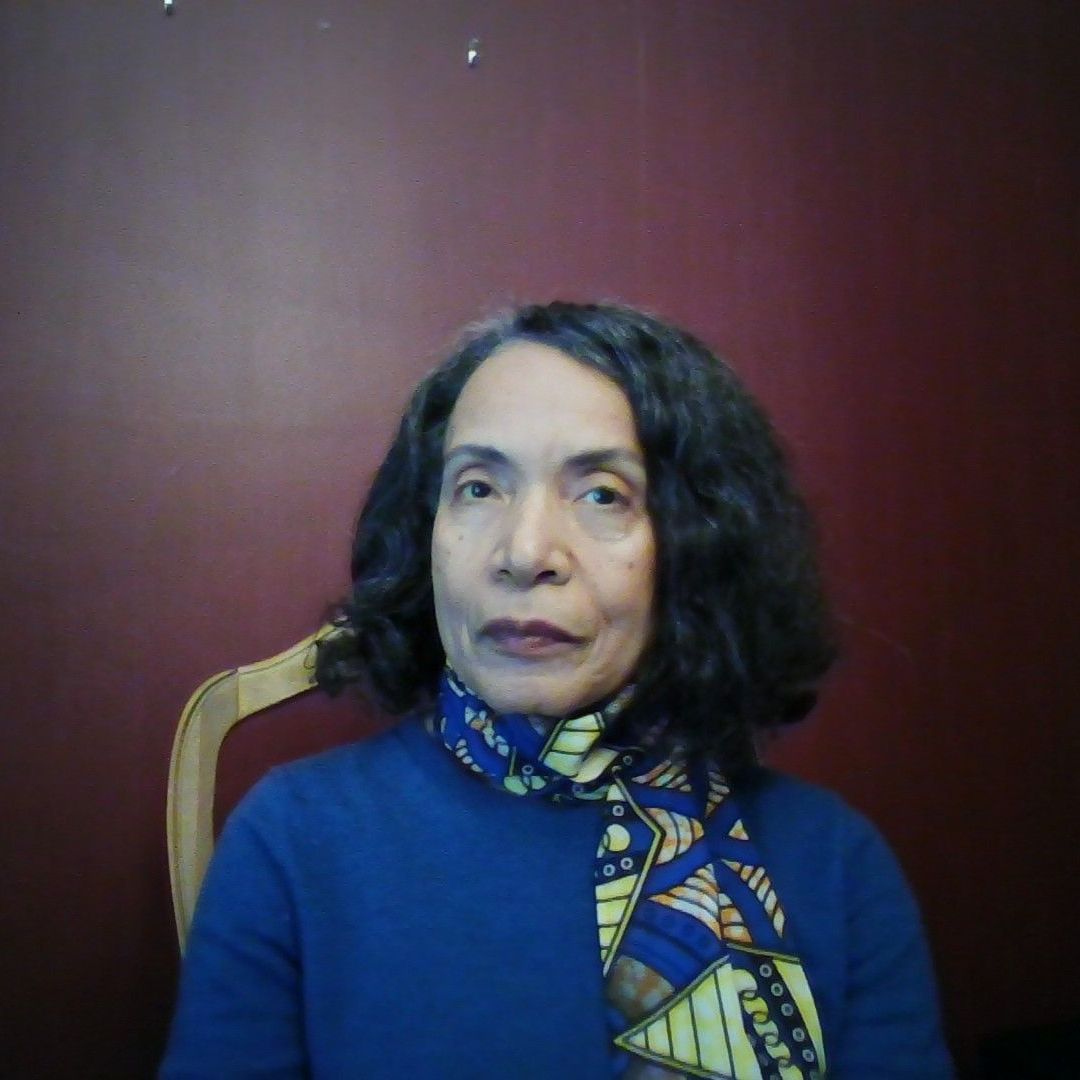 A woman wearing a blue sweater and a scarf is sitting in a chair.
