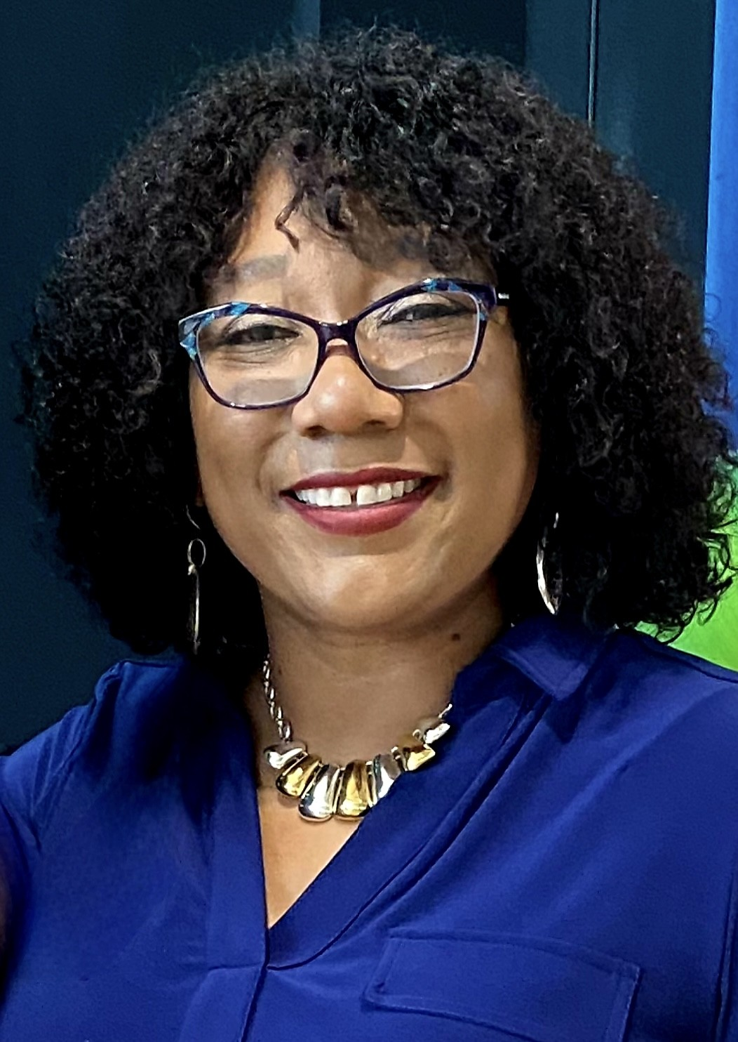 A woman wearing glasses and a blue shirt is smiling for the camera.