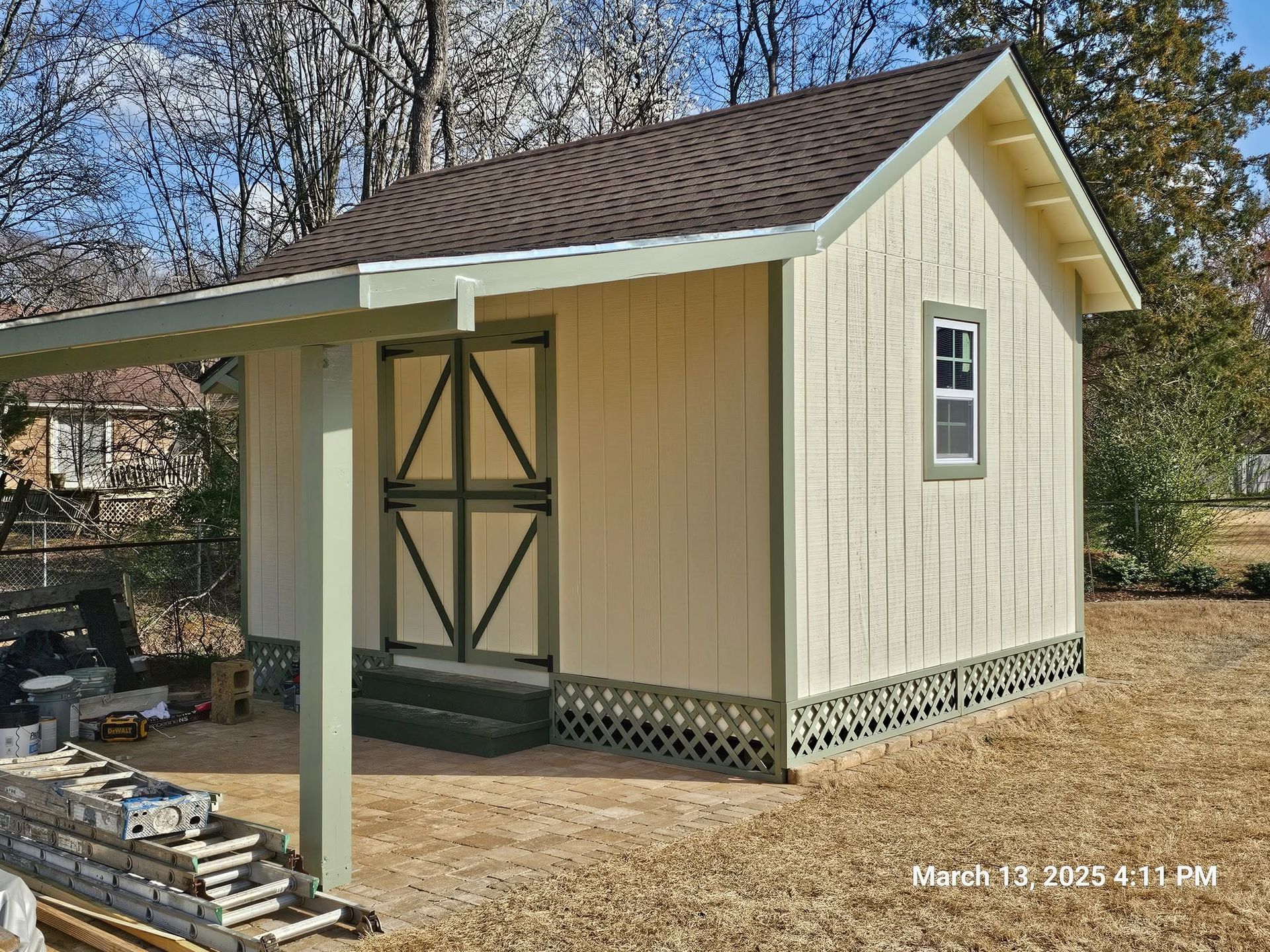 Small beige shed with green trim and front porch in a wooded yard