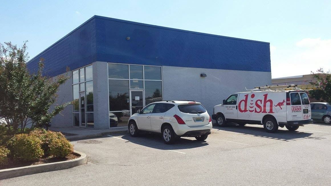 White SUV and delivery van parked outside a blue-roofed commercial building on a sunny day