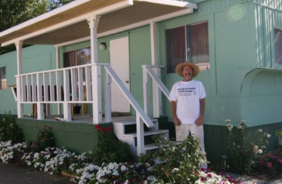 Person standing by white steps on a pastel green porch with flowers in front