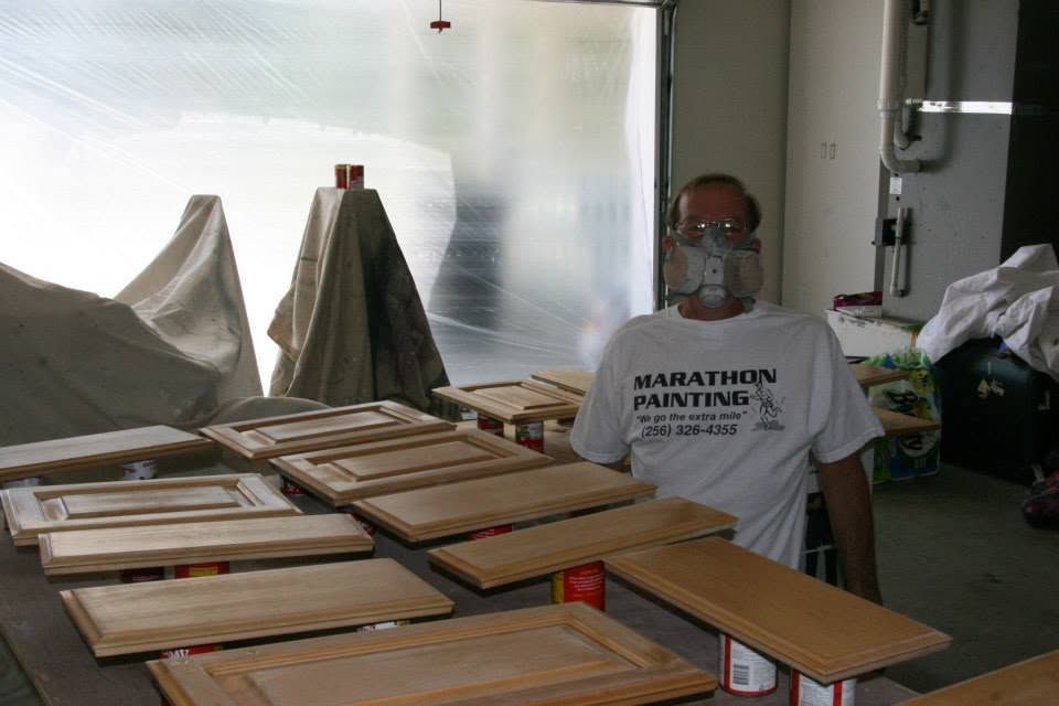 Worker in white T-shirt stands beside rows of wooden cabinet doors in a workshop