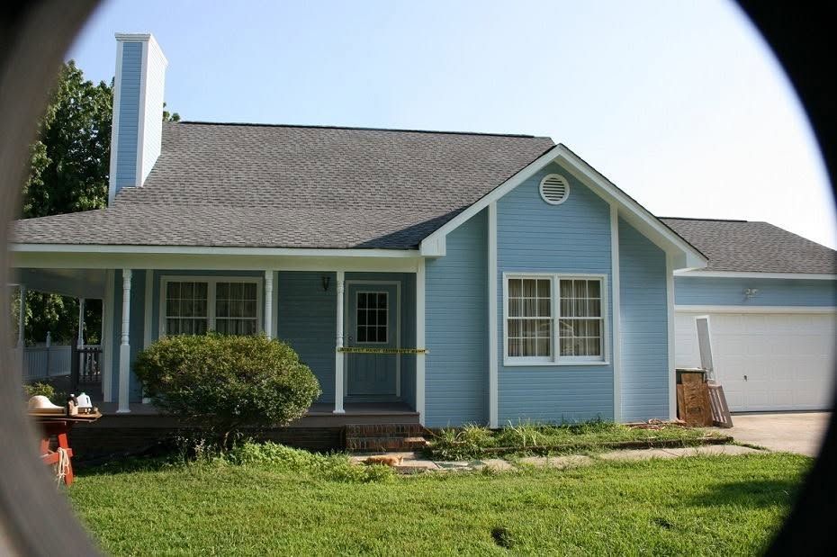 Light blue single-story house with white trim, front porch, and attached garage on a sunny day