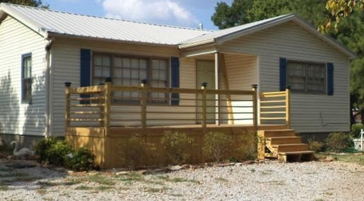 Single-story beige house with a wooden front porch and steps on a gravel driveway