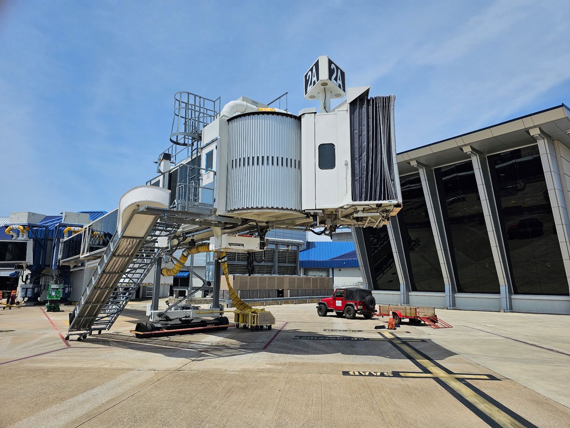 Jet bridge connecting to an airport terminal under a blue sky, with stairs and service equipment below