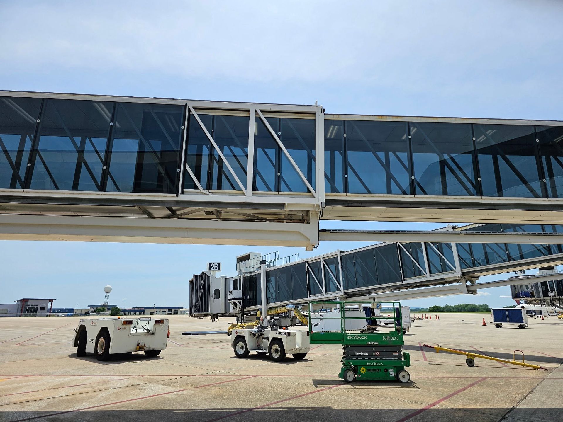 Jet bridge being towed on an airport tarmac by two vehicles under a clear blue sky