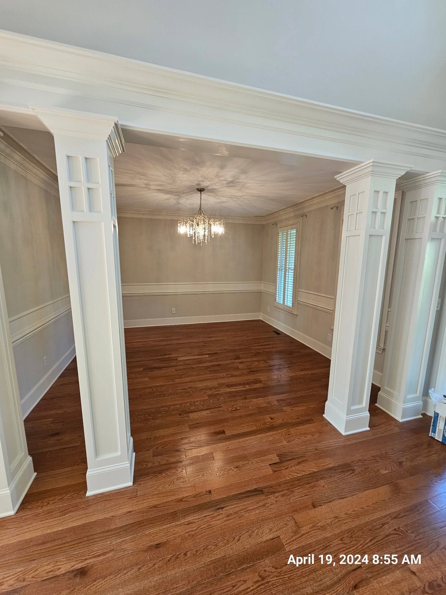 Empty formal dining room with hardwood floors, white columns, and a chandelier under recessed trim.