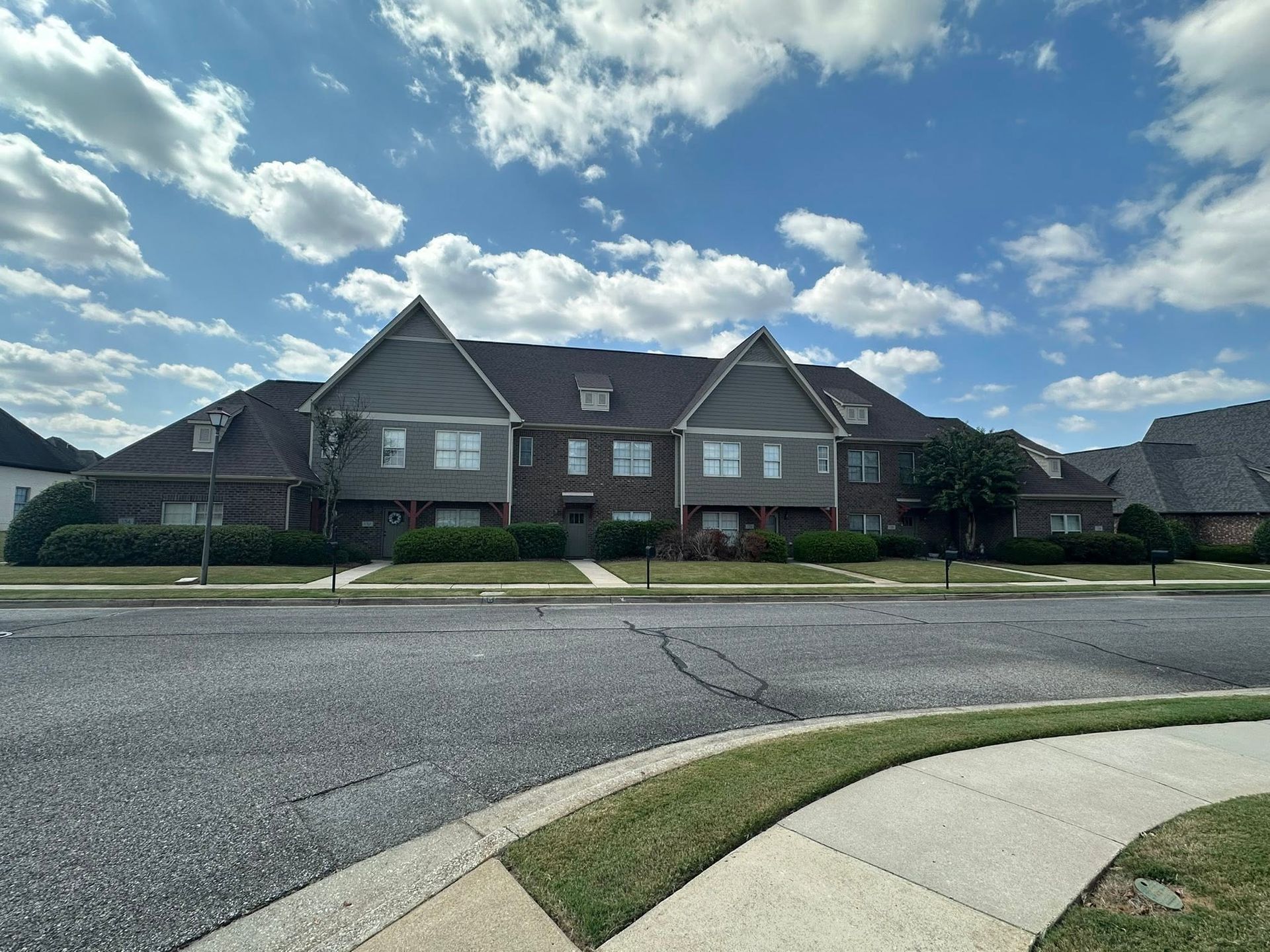 Suburban street with row houses beneath a cloudy blue sky, seen from a curved sidewalk and road.