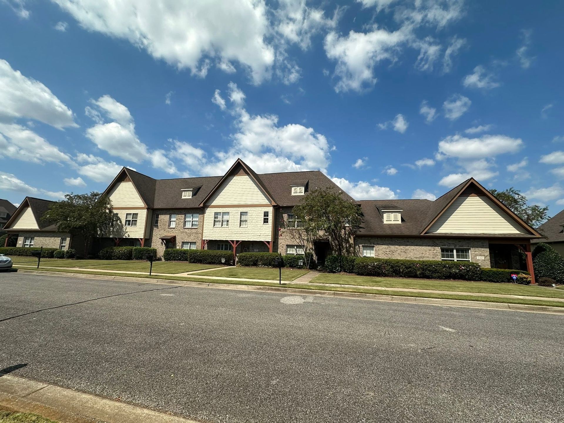 Row of beige houses with dark roofs beneath a blue sky with scattered clouds, viewed from the street.