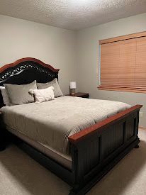 Bedroom with a dark wood bed, beige bedding, and a window with wooden blinds.